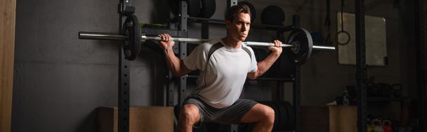 concentrated man working out with barbell in sports center, banner - Photo, Image