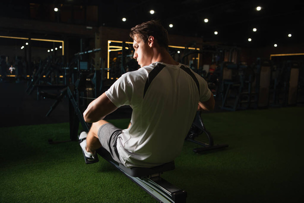 back view of man training on pull rope exercising machine in sitting pose - Fotó, kép