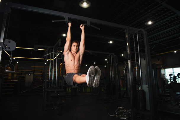 full length view of shirtless sportsman exercising on horizontal bar in gym - Foto, afbeelding