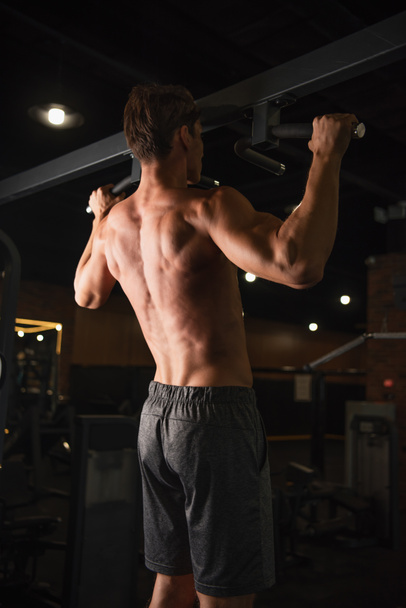 Rückenansicht des hemdslosen athletischen Mannes beim Training am Reck im Sportzentrum - Foto, Bild