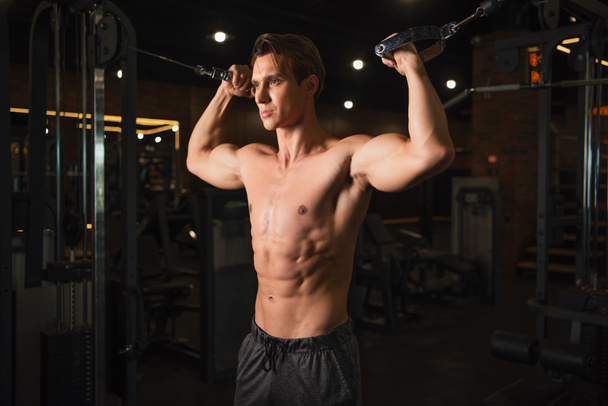 bez košile, svalnatý muž trénink na vytáhnout kabel cvičení stroj v tělocvičně - Fotografie, Obrázek