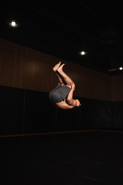 barefoot and shirtless gymnast doing somersault while training in gym - Valokuva, kuva