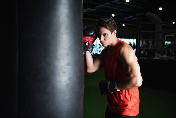 sportovec v boxerských rukavicích trénink s boxovací pytel v tělocvičně - Fotografie, Obrázek