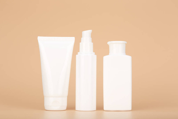 Set of white unbranded cosmetic tubes for face and body care in a row against pastel beige background. Concept of organic, natural, eco friendly cosmetics and beauty products for daily skin care - Photo, image