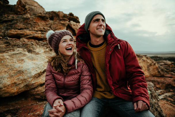 Кавказский мужчина и женщина смеются вместе, сидя в горах и наслаждаясь природой - Фото, изображение