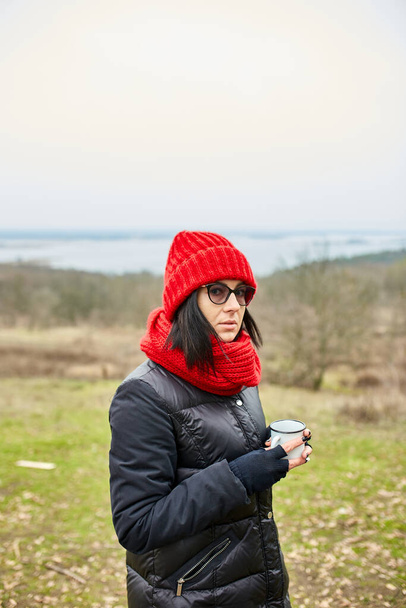 Kobieta w czerwonym kapeluszu i szaliku, picie herbaty z kubka metalu zewnątrz, Koncepcja podróży, Jesienny krajobraz tła. - Zdjęcie, obraz