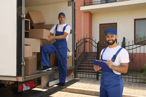 Moving service workers outdoors, unloading boxes and checking list - 写真・画像