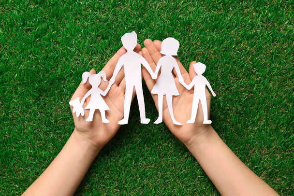 Woman holding family paper cutout on green grass, top view - Foto, Imagen