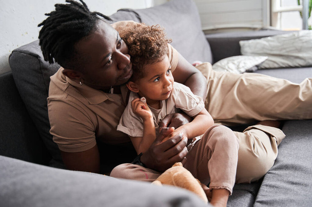 Man laying at the sofa with his daughter and looking at something attentively - Foto, imagen