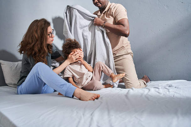 Diverse parents and their female kid sitting at the bed an playing at the funny game - Foto, immagini