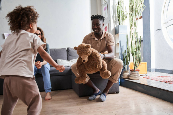 Happy young parents playing with their daughter with teddy bear at home - Fotografie, Obrázek