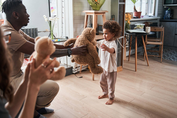 Happy young parents playing with their daughter with teddy bear at home - Fotó, kép