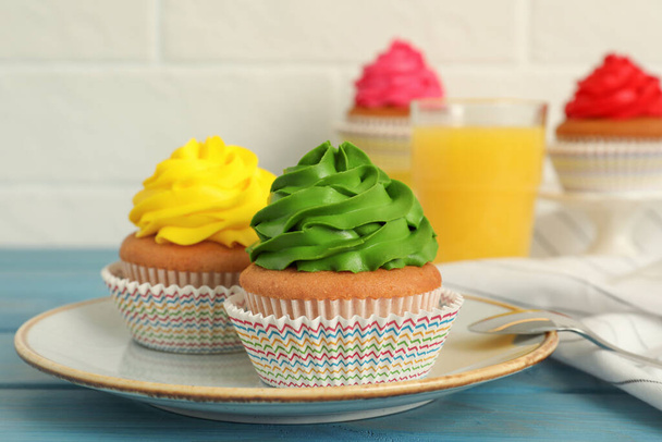 Delicious cupcakes with colorful cream on light blue wooden table - Foto, Imagen