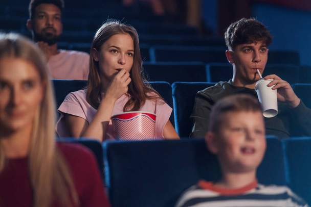 Front view of cheerful young couple with drink and popcorn in the cinema, watching film. - Fotó, kép