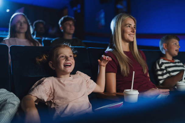 Mother with happy small children in the cinema, watching film. - Фото, изображение