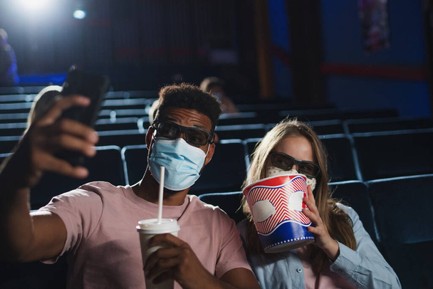 Jovem casal alegre com pipocas e óculos 3d levando selfie no cinema, conceito coronavírus. - Foto, Imagem