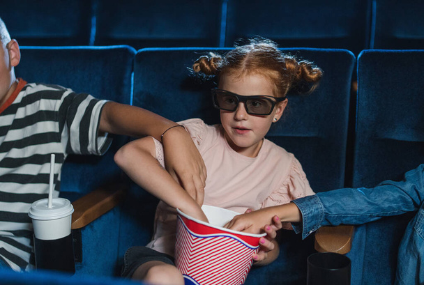 Happy small children with 3d glasses in the cinema, watching film and eating popcorn. - Фото, зображення