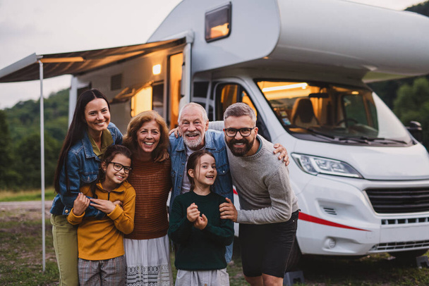 Multi-generation family looking at camera outdoors at dusk, caravan holiday trip. - Photo, image