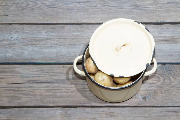 Raw potatoes in a yellow saucepan on a wooden table. - Foto, afbeelding