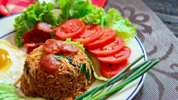 Смажений рис з китайською ковбасою подається в білій тарілці зі смаженим яйцем, помідорами та салатом
. - Фото, зображення