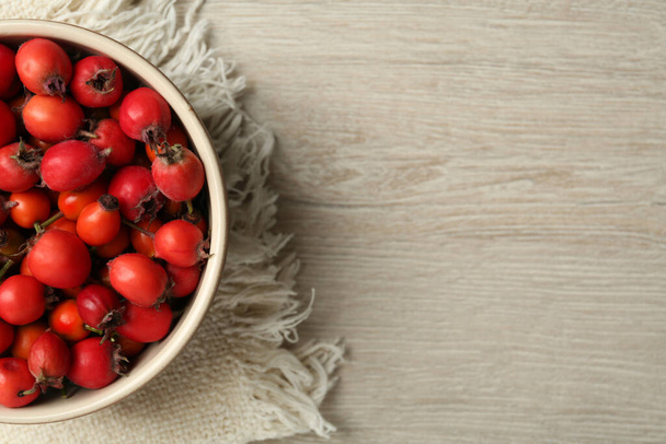Ripe rose hip berries in bowl on wooden table, top view. Space for text - Foto, Imagen