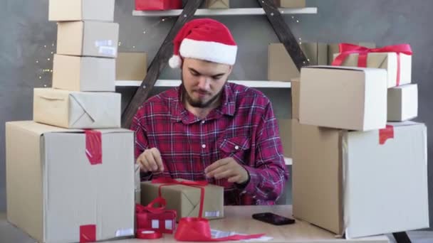 Caucasian male small business owner sitting in home office wearing santa claus hat answers a customers call. christmas sale concept. - Footage, Video