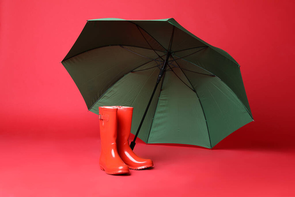 Open green umbrella and rubber boots on red background - Zdjęcie, obraz