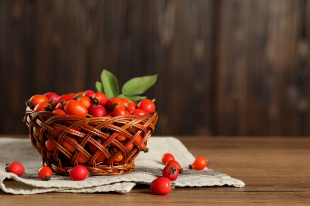 Ripe rose hip berries with green leaves on wooden table. Space for text - Foto, afbeelding
