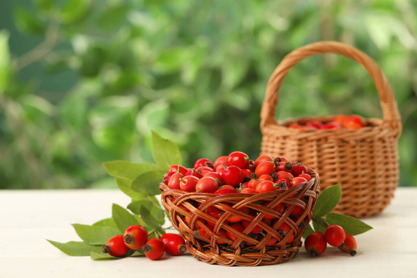 Ripe rose hip berries with green leaves on white wooden table outdoors - Fotografie, Obrázek