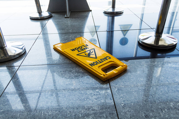 jel gondosan nedves padló fekszik a repülőtér padlóján, világos sárga jel figyelmeztetés nedves padló - Fotó, kép