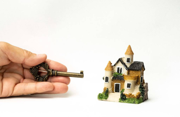 Ένα σπίτι μοντέλο και ένα κλειδί στο ανθρώπινο χέρι και στοίβα από κέρματα και να απομονώσει σε λευκό φόντο. Ιδέες έννοιας για το σχέδιο οικονομικής στέγασης. Ιδέες Concept, Αποθήκευση για ένα νέο σπίτι. - Φωτογραφία, εικόνα