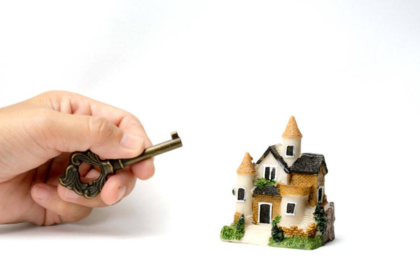 Ein Musterhaus und ein Schlüssel auf menschlicher Hand und Stapel von Münzen und Isolate auf weißem Hintergrund. Konzeptideen für den Finanzhaushalt. Konzeptideen, Sparen für ein neues Haus. - Foto, Bild