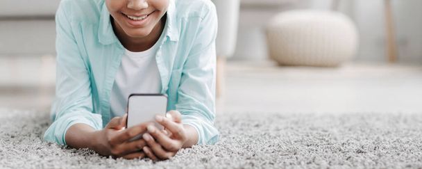 Hymyilevä teini musta tyttö katsella online-video, chattailu sosiaalisissa verkostoissa sijaitsee lattialla - Valokuva, kuva