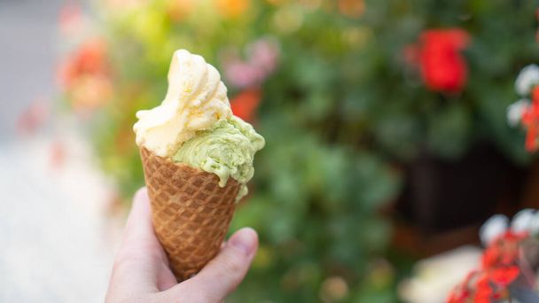Mano sosteniendo helado de doble color en cono en la calle. El mejor cono de helado. Helado de pistacho. Helado de mango - Foto, Imagen