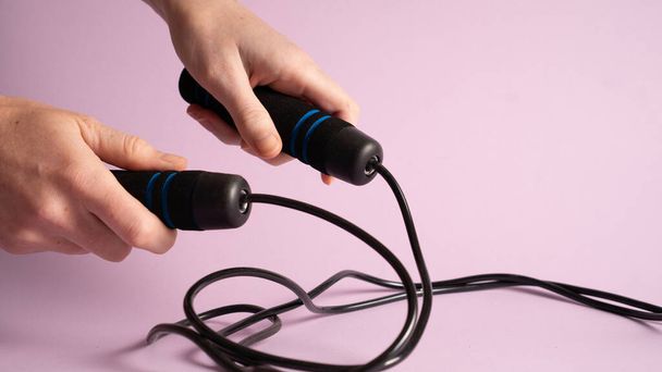 Black skipping rope in hands isolated on purple. Skipping-rope on a violet background. Jump rope in hand - 写真・画像