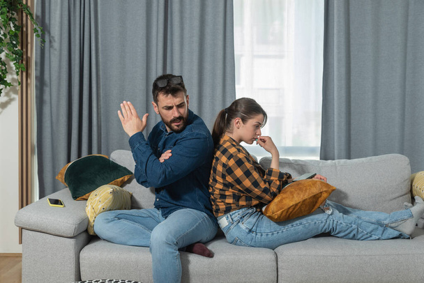 Young couple are arguing on the couch in their home and having difficulty and problems in a relationship and marriage sitting back to back and ignoring and not talking to each other - Foto, immagini