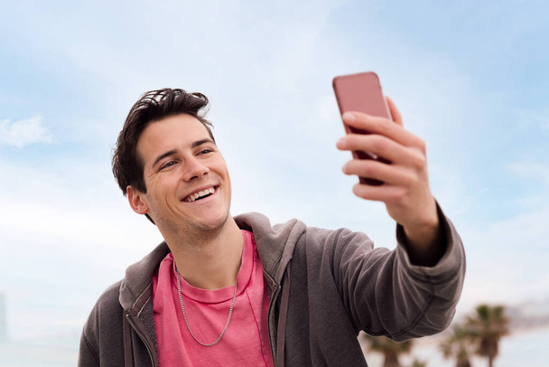 χαρούμενος νεαρός άνδρας ηχογραφεί μια βιντεοκλήση με το έξυπνο τηλέφωνό του, την έννοια της τεχνολογίας και της επικοινωνίας - Φωτογραφία, εικόνα