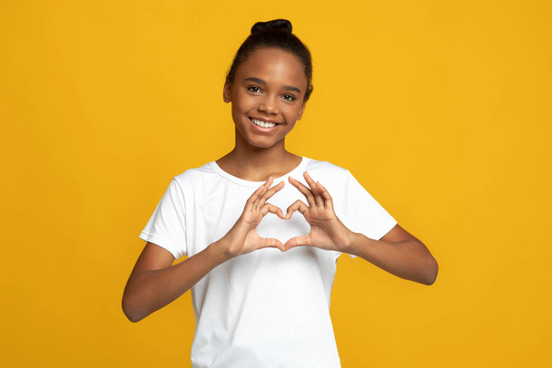 Glücklicher Teenager afrikanisch-amerikanische Schülerin Bloggerin in weißem T-Shirt zeigen Herz-Geste mit Händen - Foto, Bild