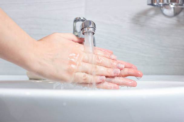 Jeune femme caucasienne se lave les mains avec de l'eau et du savon dans la salle de bain. - Photo, image