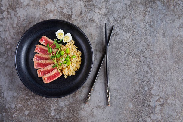 Fried pieces of tuna with kenoa and beans in a plate on a gray background. Flat lay - Fotó, kép