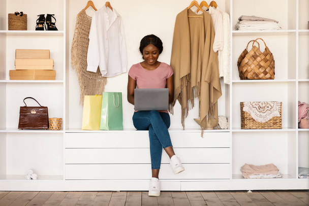 Black Female Shopaholic Using Laptop Shopping Online Purchasing Clothes Indoor - Photo, Image