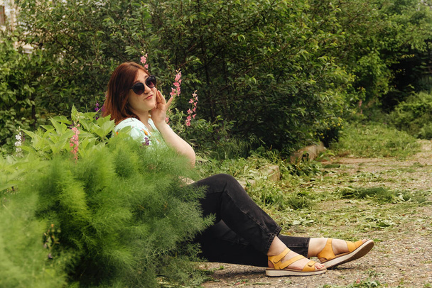 Redhead girl in a light green blouse and black jeans in greenery - Fotó, kép