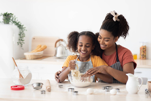 Afro-american mother showing her teen kid how to bake cookies - Фото, зображення