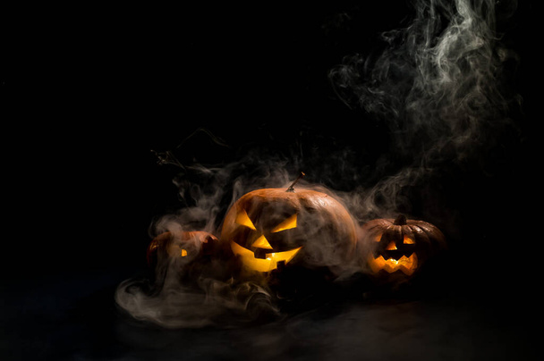 Pumpkins with carved grimaces and candles inside in the dark for halloween. Jack o latern in smoke. - Foto, imagen