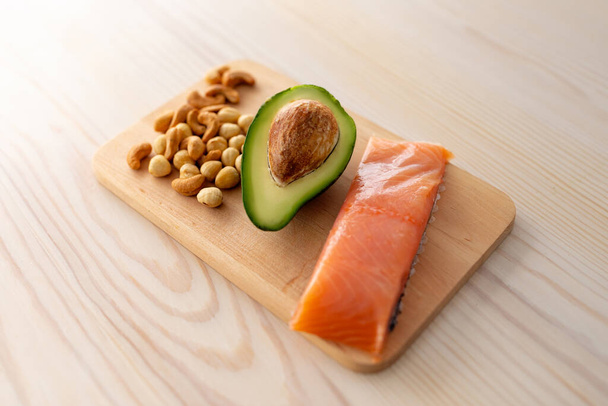 Dieta protéica e conceito de gordura saudável. Filé de salmão, metade de abacate e nozes mistas sobre tábua de corte - Foto, Imagem