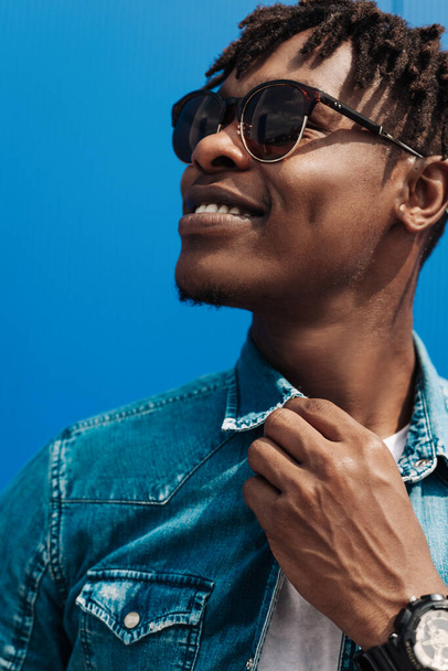 fashion african man in sunglasses in trendy modern clothes posing against the background of a blue building, on the street - Fotografie, Obrázek