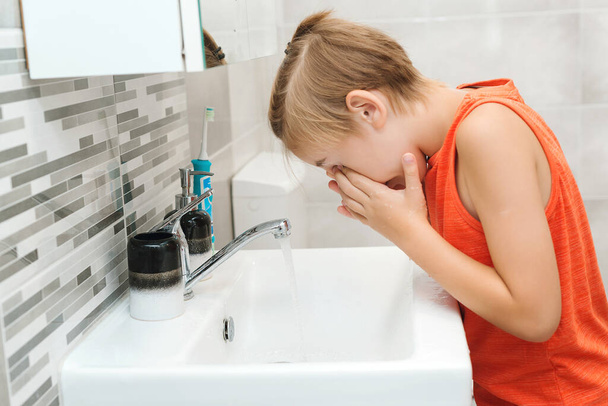 Ο έφηβος πλένεται σε νιπτήρα. Υγιής παιδική ηλικία και τρόπος ζωής. Το παιδί πλένει το πρόσωπο του στο μπάνιο. Πρωινή υγιεινή. Υγιεινή των δοντιών κάθε μέρα. Υγειονομική περίθαλψη, παιδική και οδοντιατρική υγιεινή. - Φωτογραφία, εικόνα