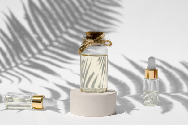 Flaschen mit natürlichen ätherischen Ölen auf weißem Hintergrund mit harten Schatten von Farnblättern. Naturkosmetik. Hautpflegekonzept - Foto, Bild
