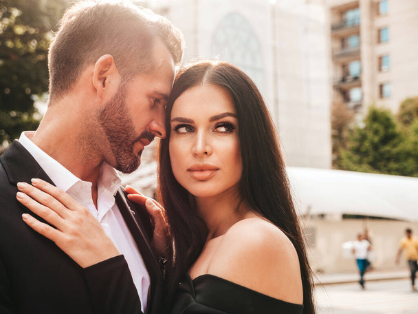 Beautiful fashion woman and her handsome elegant boyfriend in suit. Sexy brunette model in black evening dress. Fashionable couple posing in the street in Europe. Brutal man and his female outdoors - Φωτογραφία, εικόνα