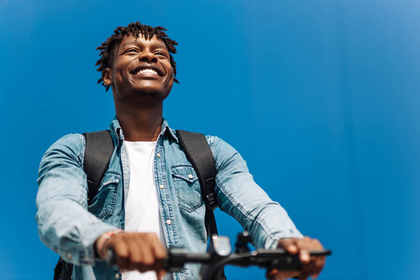 modern african american on electric scooter, business man is one to work, student is one to study, against the background of a blue building - 写真・画像
